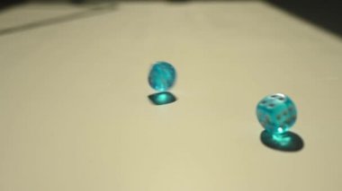 Mavi zarlar beyaz bir masaya ağır çekimde atılır.