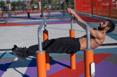 Spor sahasındaki paralel çubuklarda üstsüz adam yatay denge yapıyor.