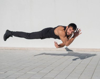 Siyah spor kıyafetli bir adam dışarıda şınav çekerken zıplıyor.