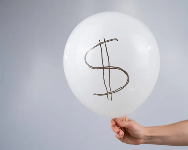 A woman is holding a balloon with a dollar sign. The concept of an inflated currency value
