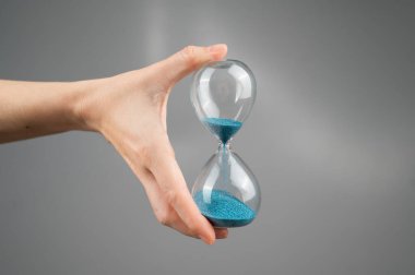 Gri arka planda kum saati tutan bir kadın. Yakın plan. Boşluğu kopyala