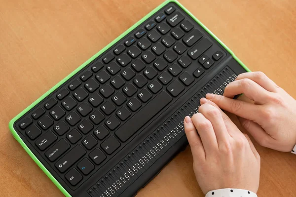 A blind woman uses a computer with a Braille display and a computer keyboard. Inclusive device