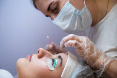 Usta, müşterilerin kirpiklerindeki katman bileşimini pamuklu bezle temizliyor. Kirpik perma prosedürü