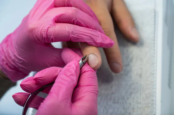 Manicurist cuts off cuticle to male client using nippers