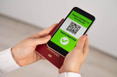 Pasaportu ve telefonu olan bir kadın aşı ile ilgili QR kodu taşıyor.