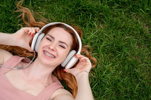 Ung Rödhårig Kvinna Ligger Gräset Och Lyssnar Musik — Stockfoto