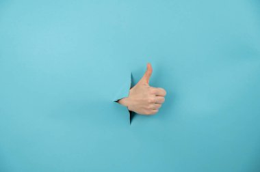 Bir kadının eli mavi arka planda bir delikten dışarı sarkan bir baş parmağını gösterir.