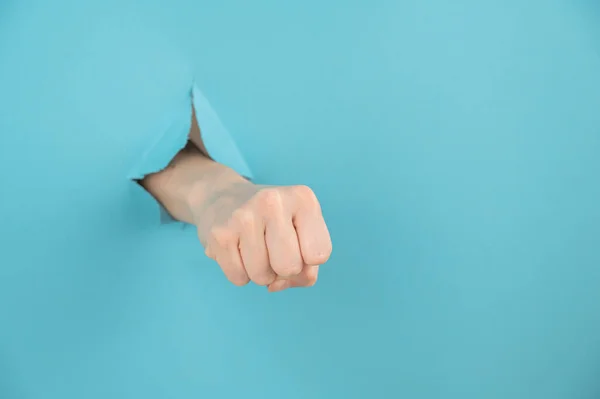 A womans hand sticking out of a hole from a blue background shows a fist