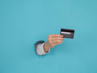 Bir kadının eli kağıtta bir delikten dışarı sarkan mavi arka planda bir kredi kartı tutar.