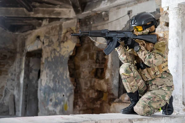 Portrait of a woman in a helmet and goggles with a machine gun in her hands. A female soldier in a camouflage uniform holds a weapon