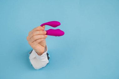 Bir kadının eli pembe bir seks oyuncağını kağıt mavisi bir arka planda bir delikten tutar.