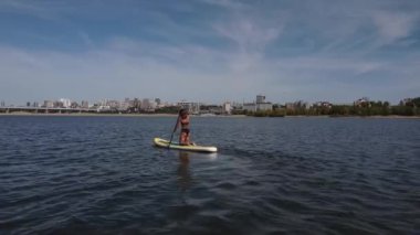 Beyaz bir kadın şehirdeki nehirde SUP sörfüne biniyor. Yaz sporu