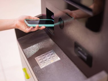 ATM 'de akıllı telefon kullanan bir kadın. NFC çevrimiçi bankacılık kavramı