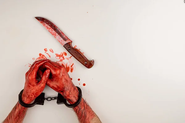 ナイフの横にある白いテーブルの上に血のついた手錠をかけた男が — ストック写真