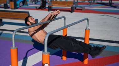 Spor sahasındaki paralel çubuklarda üstsüz adam yatay denge yapıyor.