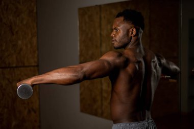 Çekici Afrikalı Amerikalı adam dambıllarla kol egzersizi yapıyor.