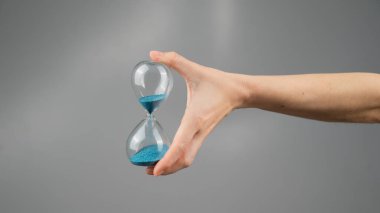 Gri arka planda kum saati tutan bir kadın. Yakın plan. Boşluğu kopyala