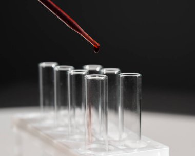 Laboratuvar asistanının, pipetten kan damlatarak test tüpüne kan damlattığı yakın plan.
