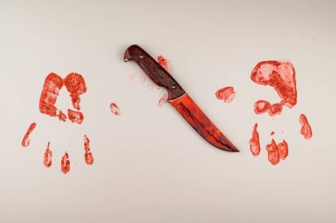 Kanlı bıçak ve el izleri beyaz bir masada.