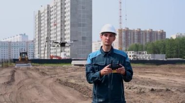 Kasklı ve tulumlu bir adam inşaat alanındaki bir dronu kontrol ediyor. İnşaatçı teknik bir hata yapıyor.