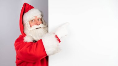Noel Baba beyaz arka plandaki bir reklamın arkasından bakar. Mutlu Noeller.
