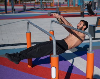Spor sahasındaki paralel çubuklarda üstsüz adam yatay denge yapıyor.