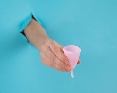 Mavi arka planda bir delikten dışarı sarkan bir kadın eli pembe bir adet bardağı tutuyor.