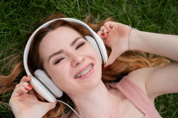 Ung Rödhårig Kvinna Ligger Gräset Och Lyssnar Musik — Stockfoto