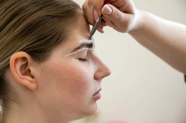 The master draws the shape of the eyebrows with white paint before coloring