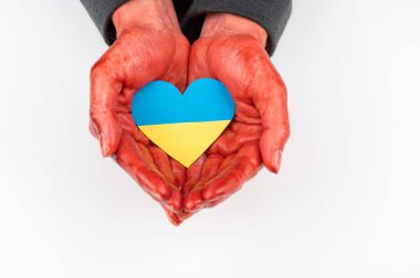 Elleri kana bulanmış bir kadın beyaz arka planda Ukrayna bayrağı taşıyan bir kalp tutuyor.