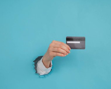 Bir kadının eli kağıtta bir delikten dışarı sarkan mavi arka planda bir kredi kartı tutar.