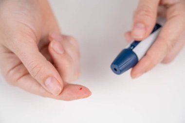 Beyaz bir kadın kalem mızrağı kullanarak glikoz testi yapıyor.