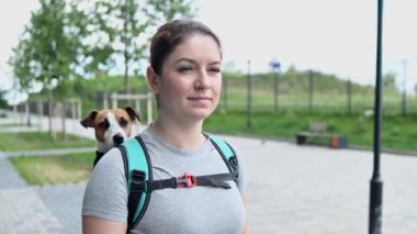 Beyaz bir kadın özel bir sırt çantasıyla köpek Jack Russell Terrier ile dışarı çıkıyor.