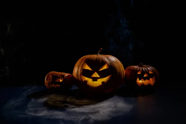 Pumpkins with carved grimaces and candles inside in the dark for halloween. Jack o latern in smoke