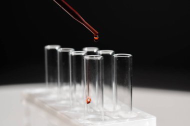 Laboratuvar asistanının, pipetten kan damlatarak test tüpüne kan damlattığı yakın plan.