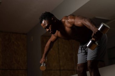 Çekici Afrikalı Amerikalı adam dambıllarla kol egzersizi yapıyor.