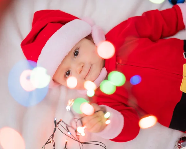 Chłopiec Ubrany Strój Mikołaja Leży Łóżku Bawi Się Świąteczną Girlandą — Zdjęcie stockowe