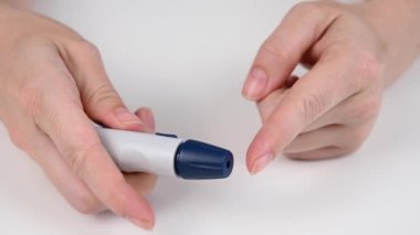 Beyaz bir kadın kalem mızrağı kullanarak glikoz testi yapıyor.