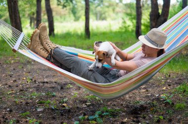 Beyaz kadın bir hamakta Jack Russell Terrier köpeğiyle çam ormanında yatıyor..