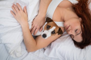 Kafkasyalı kadın yatağında uyuyor sevgili köpeğine sarılıyor.