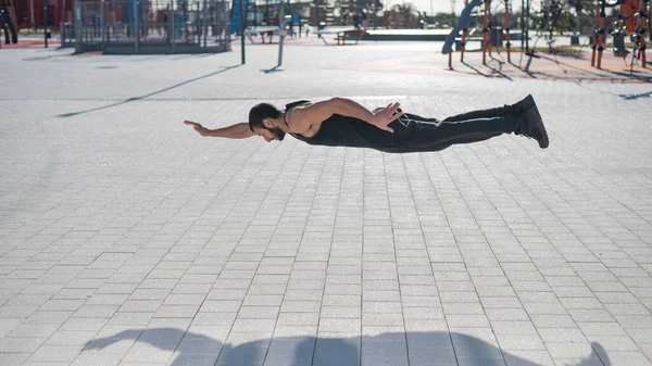 A man in black sportswear jumps doing push-ups in the park