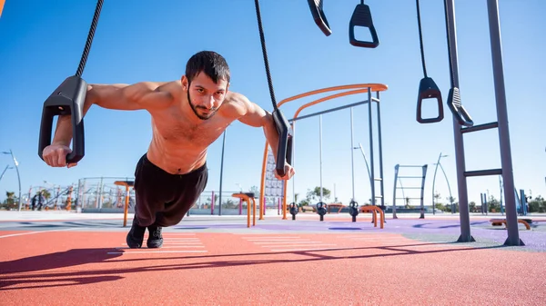 Tişörtsüz adam dışarıda ilmek egzersizi yapıyor.