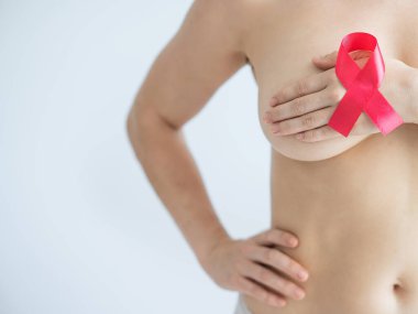 Beyaz bir arka planı olan beyaz bir kadın göğsünü kapatıyor. Pembe kurdele göğüs kanseriyle mücadeleyi sembolize ediyor.