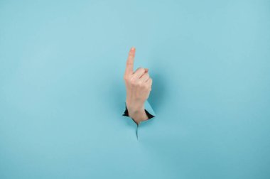Bir kadının eli mavi arka planda bir delikten dışarı sarkan işaret parmağını gösterir.
