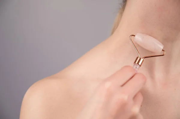 Close-up portrait of a woman using a quartz roller massager for an alternative fight against wrinkles on her neck. Smoothing of the rings of venus