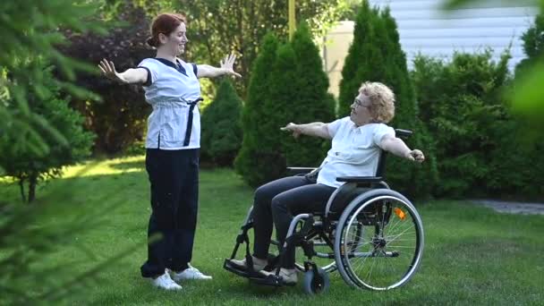 一位护士正在外面和一位坐在轮椅上的老年病人一起锻炼 — 图库视频影像