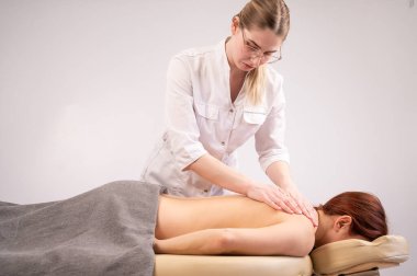 Doktor, kadın bir hastanın sırtına masaj yapıyor. 