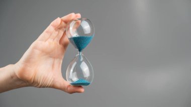 Gri arka planda kum saati tutan bir kadın. Yakın plan. Boşluğu kopyala