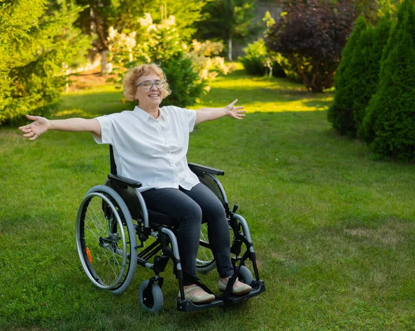 快乐的老妇人坐在轮椅上散步时 把胳膊伸向两边 — 图库照片