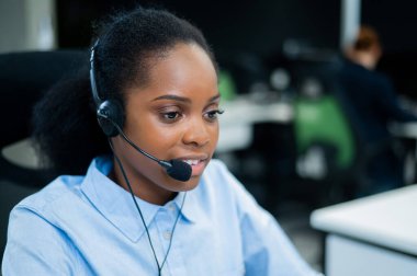 Afrikalı genç bir kadın kulaklıkla bir müşteriyle konuşuyor. Çağrı merkezinin kadın çalışanı